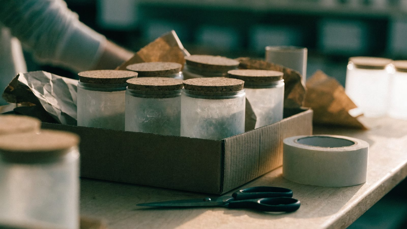 Glass candle jars with cork lids being packed into a carton at a packing bench